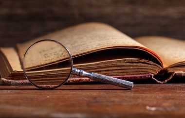 Vintage book and magnifying glass on wooden background