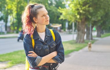 Serious teen schoolgirl with backpack, hands crossed, outdoor, copy space